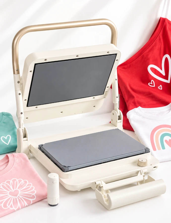 Plancha térmica Silhouette Cloché abierta junto a prendas personalizadas y accesorios.